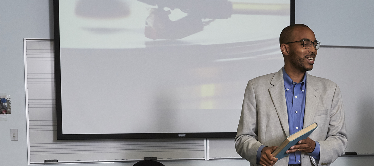 A professor at the front of a class is holding a book