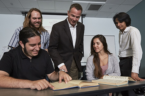 A professor with a group of students are looking down at something